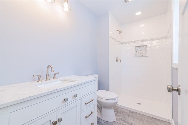 bathroom with vanity, tiled shower, and toilet