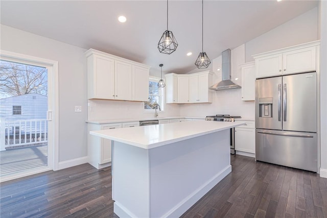 kitchen featuring vaulted ceiling, decorative light fixtures, white cabinets, stainless steel appliances, and wall chimney exhaust hood