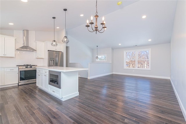 kitchen featuring hanging light fixtures, appliances with stainless steel finishes, wall chimney range hood, and white cabinets