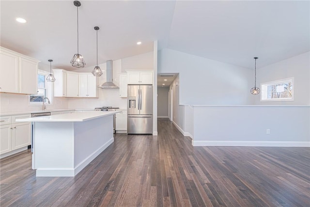 kitchen with white cabinetry, wall chimney range hood, stainless steel fridge, and decorative light fixtures