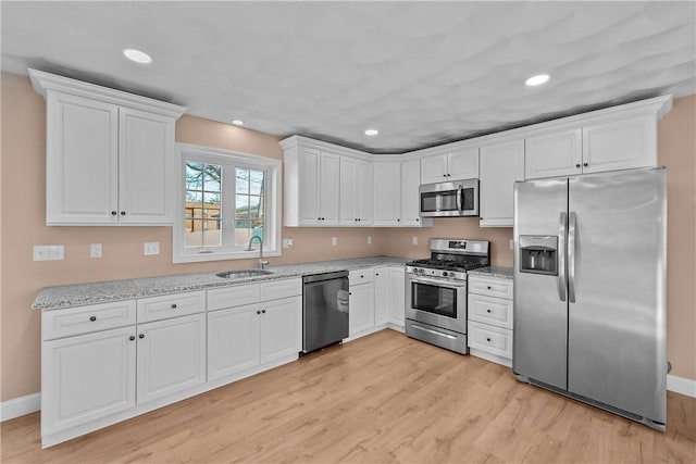 kitchen with sink, appliances with stainless steel finishes, white cabinetry, light hardwood / wood-style floors, and light stone countertops