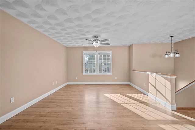 unfurnished living room with ceiling fan with notable chandelier and light hardwood / wood-style flooring