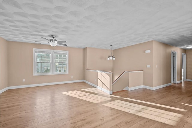 empty room with ceiling fan with notable chandelier and light hardwood / wood-style flooring