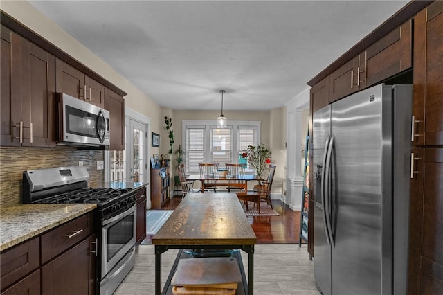 kitchen with light stone counters, decorative light fixtures, dark brown cabinets, stainless steel appliances, and decorative backsplash