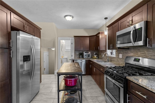 kitchen with sink, light stone counters, hanging light fixtures, appliances with stainless steel finishes, and decorative backsplash