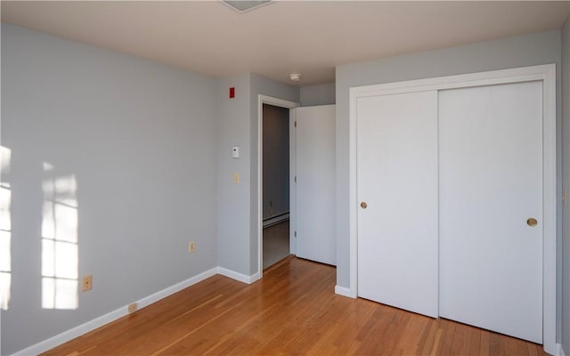 unfurnished bedroom featuring baseboard heating, a closet, and light wood-type flooring