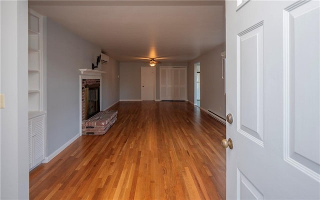 unfurnished living room featuring light hardwood / wood-style flooring, ceiling fan, a baseboard heating unit, a brick fireplace, and built in shelves