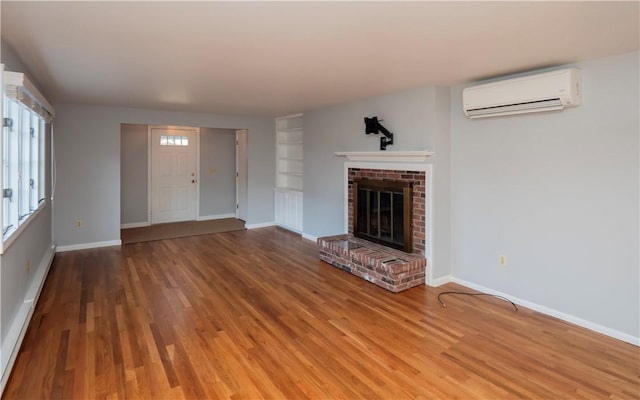 unfurnished living room with a wall mounted AC, hardwood / wood-style floors, and a brick fireplace