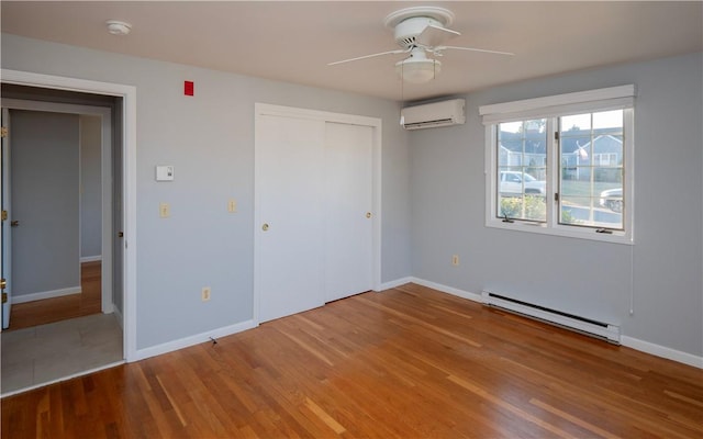 unfurnished bedroom featuring a wall mounted AC, baseboard heating, a closet, ceiling fan, and hardwood / wood-style floors