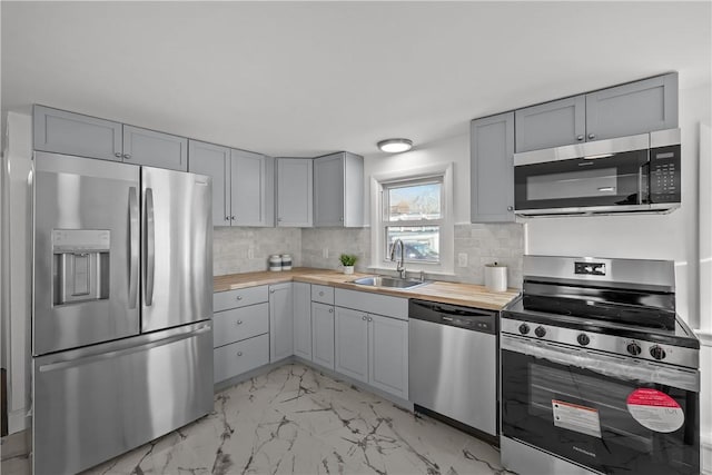 kitchen featuring appliances with stainless steel finishes, wood counters, tasteful backsplash, sink, and gray cabinetry