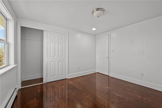 unfurnished bedroom featuring dark wood-type flooring, a baseboard radiator, and a closet