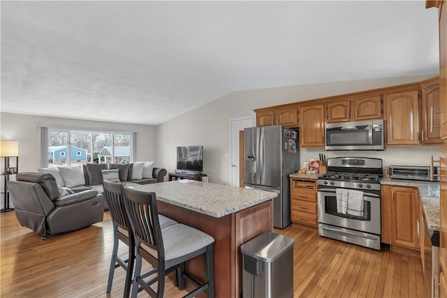 kitchen featuring vaulted ceiling, appliances with stainless steel finishes, a breakfast bar area, and light wood-type flooring