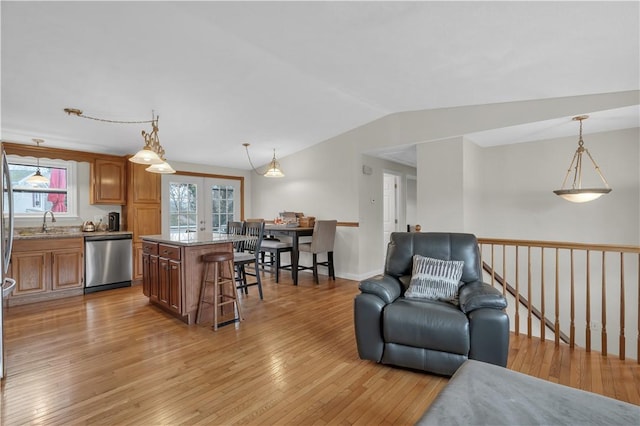 kitchen featuring hanging light fixtures, a kitchen island, a kitchen bar, stainless steel dishwasher, and light wood-type flooring