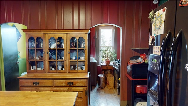 interior space with black refrigerator with ice dispenser, stainless steel gas range oven, and wood walls