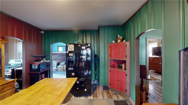 kitchen with gas range, black refrigerator with ice dispenser, and wood walls