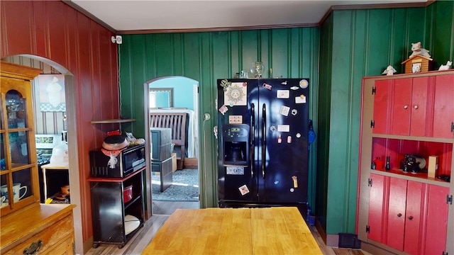 kitchen with hardwood / wood-style flooring, black fridge with ice dispenser, and wood walls