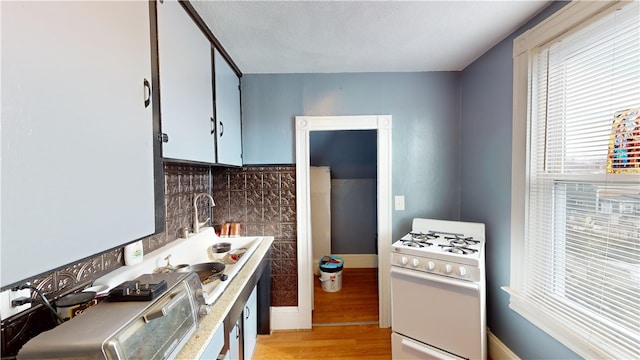 kitchen with backsplash, light hardwood / wood-style floors, and gas range gas stove