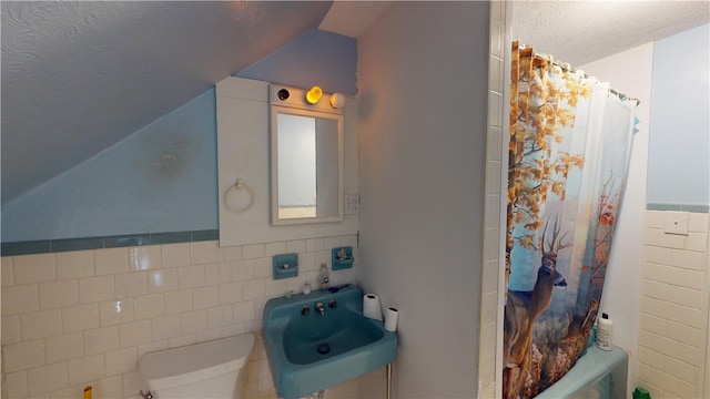 full bathroom with toilet, sink, vaulted ceiling, tile walls, and a textured ceiling