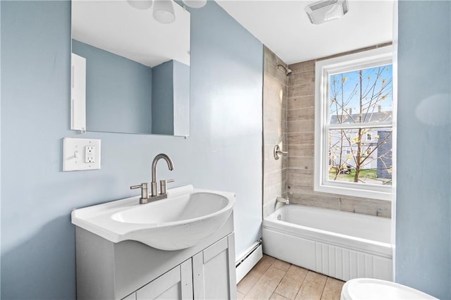 full bathroom featuring tiled shower / bath combo, vanity, a baseboard heating unit, and toilet