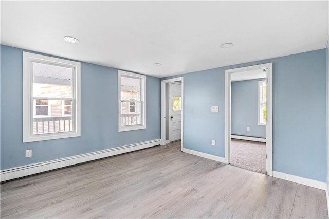 empty room with light hardwood / wood-style floors, a healthy amount of sunlight, and baseboard heating