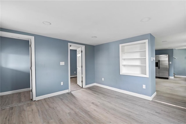 spare room featuring built in shelves, baseboard heating, and light wood-type flooring