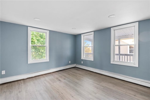 spare room featuring a baseboard heating unit, a healthy amount of sunlight, and light wood-type flooring