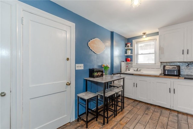 kitchen featuring white cabinetry, wood-type flooring, sink, and tasteful backsplash