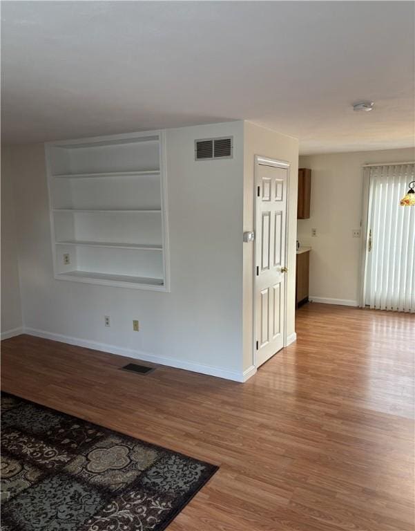 empty room with built in shelves and light wood-type flooring