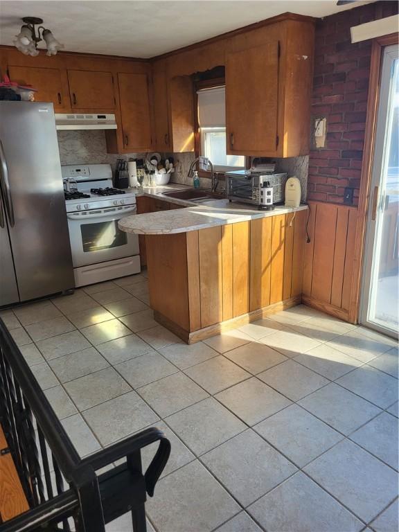 kitchen with sink, light tile patterned floors, stainless steel fridge, kitchen peninsula, and white gas range oven