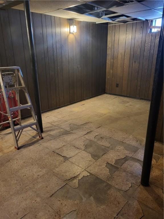 basement with a drop ceiling and wood walls