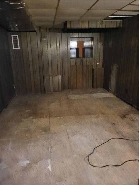 basement with a paneled ceiling and wood walls