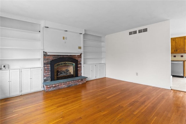 unfurnished living room with built in shelves, a fireplace, and light hardwood / wood-style floors