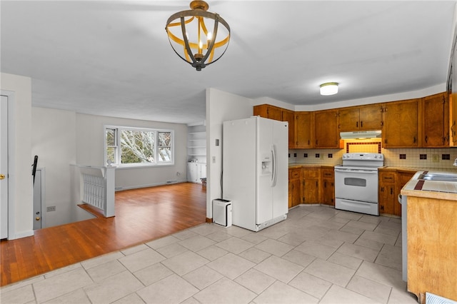 kitchen with tasteful backsplash, a chandelier, pendant lighting, white appliances, and light hardwood / wood-style floors