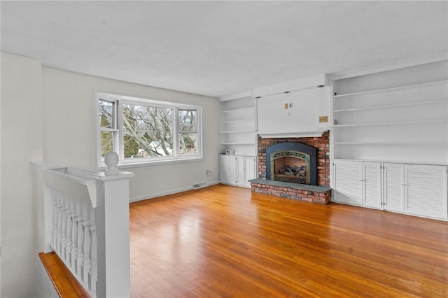 unfurnished living room with a brick fireplace, light hardwood / wood-style flooring, and built in features