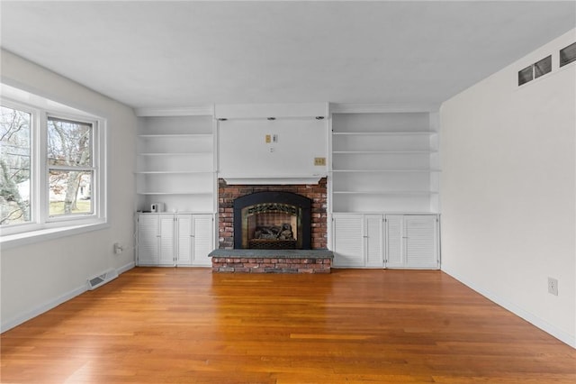 unfurnished living room with built in shelves, wood-type flooring, and a fireplace