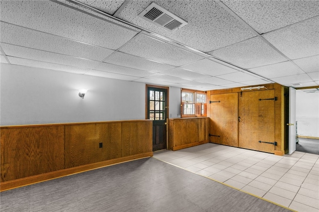 basement featuring a paneled ceiling and wooden walls