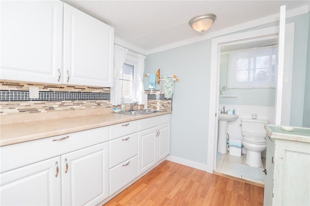 interior space with sink, decorative backsplash, light hardwood / wood-style flooring, and white cabinets