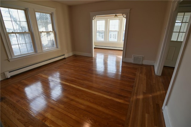 empty room with a baseboard radiator, visible vents, baseboard heating, wood finished floors, and baseboards