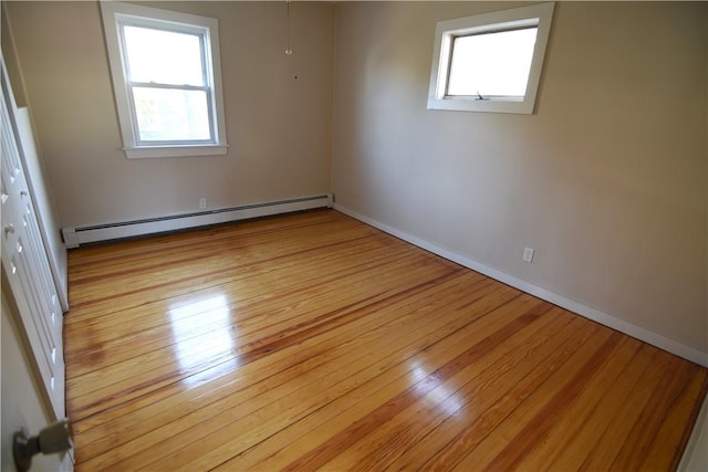 unfurnished room with a baseboard heating unit, a wealth of natural light, and light wood finished floors