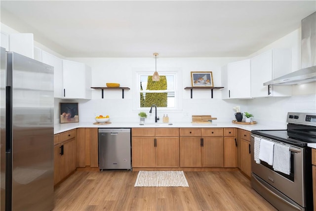 kitchen featuring wall chimney exhaust hood, sink, hanging light fixtures, appliances with stainless steel finishes, and white cabinets