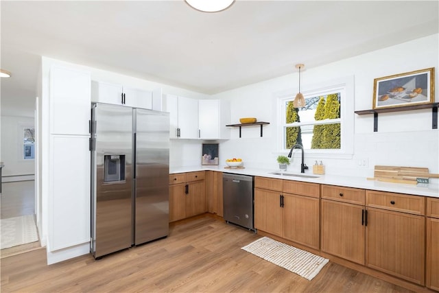 kitchen with white cabinetry, sink, hanging light fixtures, light hardwood / wood-style floors, and stainless steel appliances