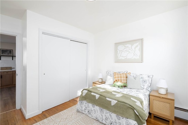 bedroom with hardwood / wood-style flooring, a closet, and baseboard heating