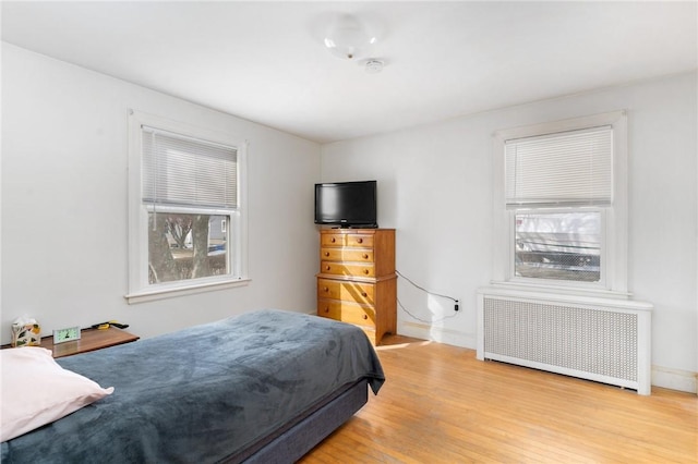 bedroom with radiator heating unit, light hardwood / wood-style floors, and multiple windows