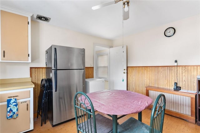 dining space with ceiling fan, wood walls, and light wood-type flooring