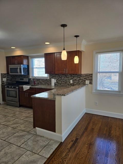 kitchen with crown molding, hanging light fixtures, dark stone countertops, kitchen peninsula, and stainless steel appliances