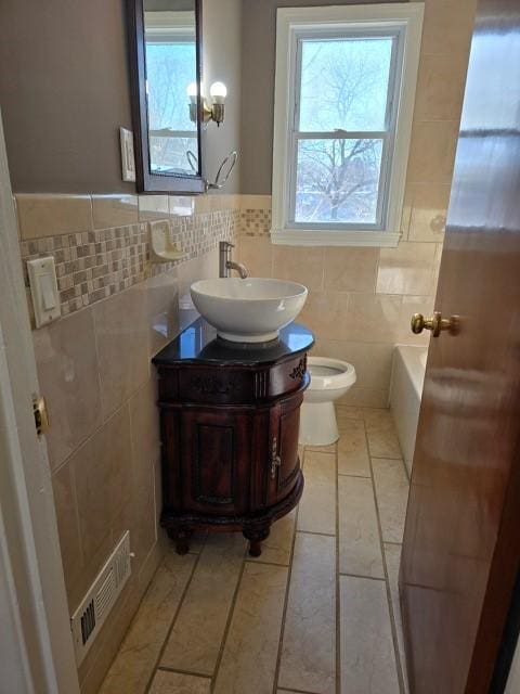 bathroom with toilet, tile walls, vanity, a tub, and tile patterned flooring