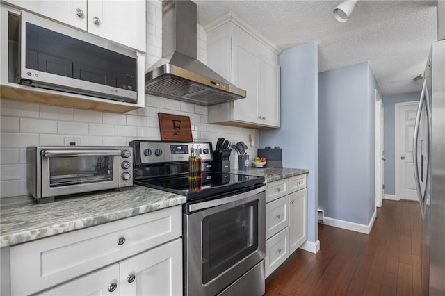 kitchen with white cabinetry, light stone counters, dark hardwood / wood-style floors, stainless steel appliances, and wall chimney range hood