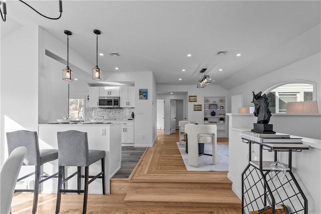 kitchen featuring built in features, tasteful backsplash, white cabinetry, hanging light fixtures, and light hardwood / wood-style floors