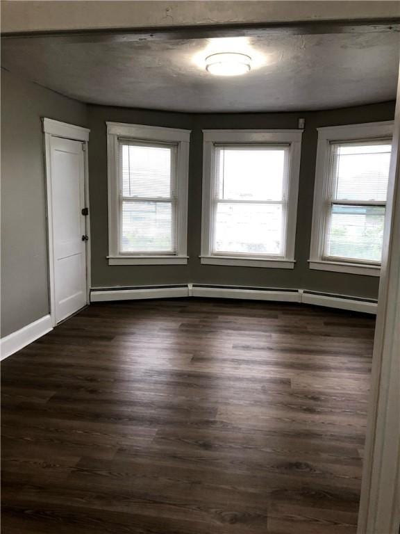 unfurnished room featuring dark wood-type flooring and a baseboard heating unit