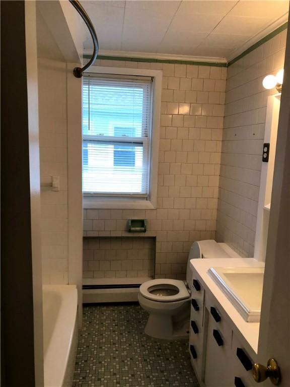 bathroom with toilet, tile walls, a baseboard radiator, vanity, and ornamental molding